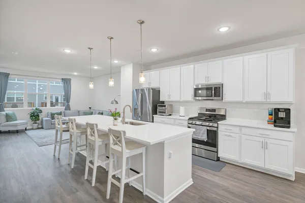 a kitchen with stainless steel appliances kitchen island granite countertop a stove a sink a refrigerator with white cabinets and wooden floor