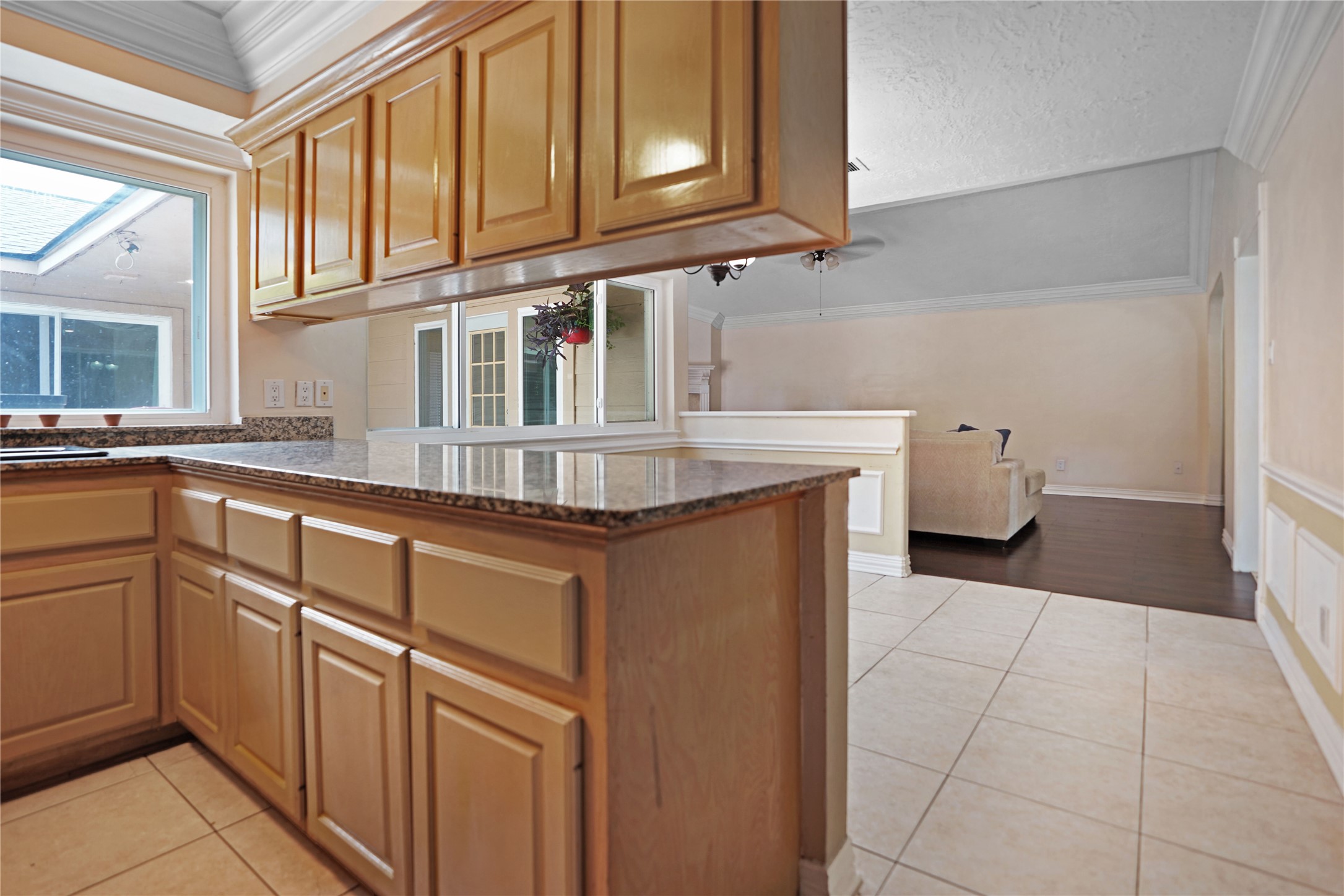 17119 Mellow Ridge Drive Spring, TX 77379 - Photo 11 of 32 This photo shows a bright kitchen with wooden cabinets, granite countertops, and tile flooring. It opens to a spacious living area with wood floors and a cozy seating arrangement, offering a seamless flow for entertaining.