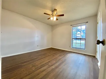 an empty room with wooden floor fan and windows