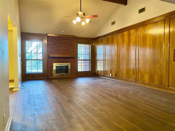 an empty room with wooden floor fireplace and windows