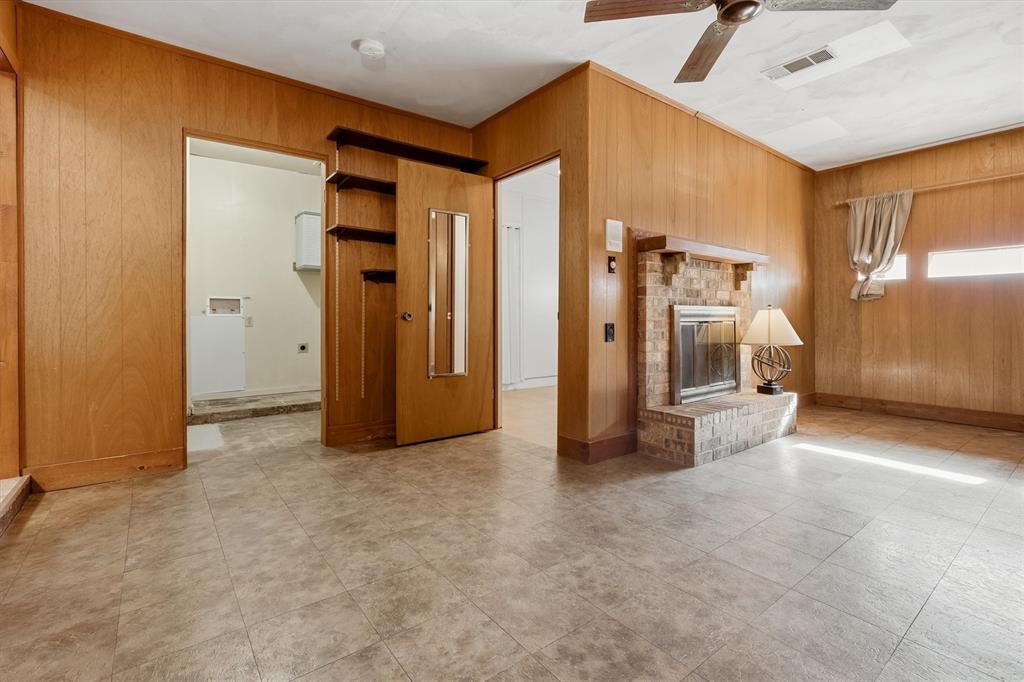 1817 Indian School Road Garland, TX 75044 - Photo 27 of 40 Unfurnished living room featuring wooden walls, a brick fireplace, and a ceiling fan