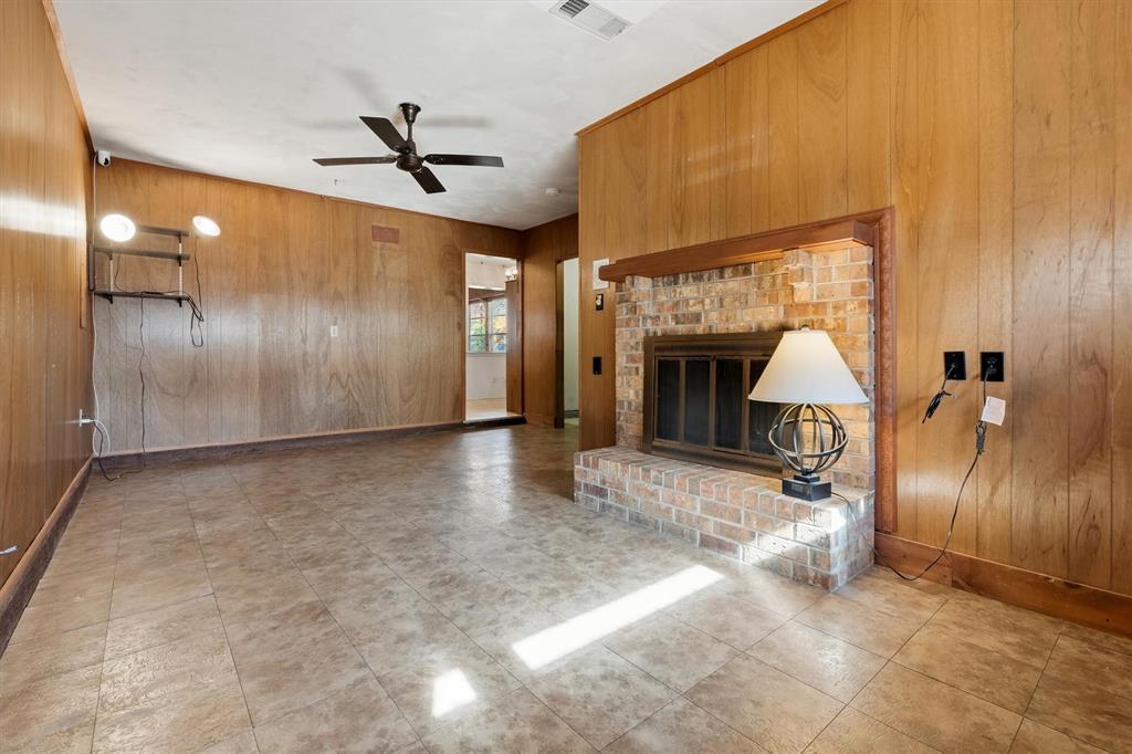 1817 Indian School Road Garland, TX 75044 - Photo 28 of 40 Unfurnished living room featuring wood walls, a brick fireplace, and ceiling fan