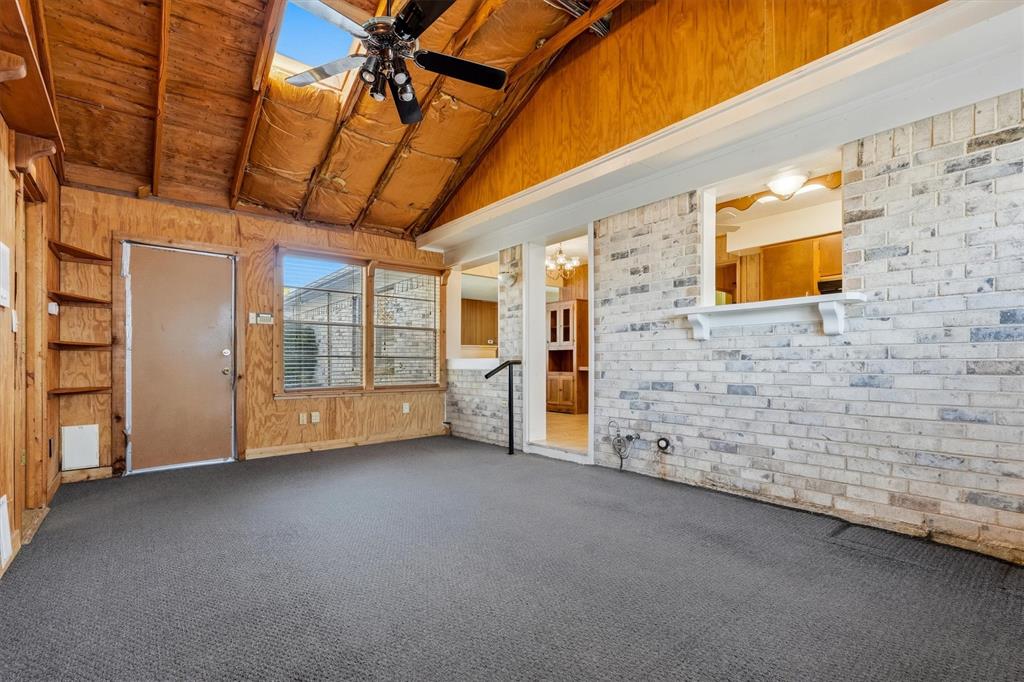 1817 Indian School Road Garland, TX 75044 - Photo 32 of 40 Unfurnished room featuring vaulted ceiling, ceiling fan, brick wall, carpet flooring, and wood walls