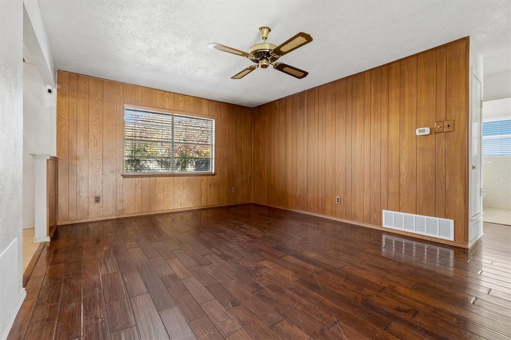 1817 Indian School Road Garland, TX 75044 - Photo 7 of 40 Unfurnished room with dark wood-style floors, ceiling fan, healthy amount of natural light, a textured ceiling, and wooden walls