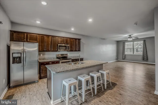 a kitchen with stainless steel appliances granite countertop a stove a sink a refrigerator white cabinets and wooden floor