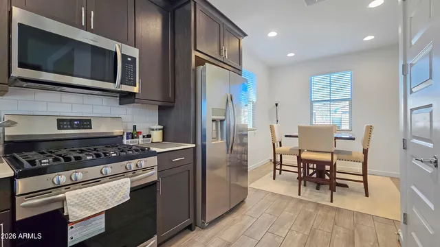 a kitchen with stainless steel appliances granite countertop a stove top oven a sink dishwasher a dining table and chairs with wooden floor