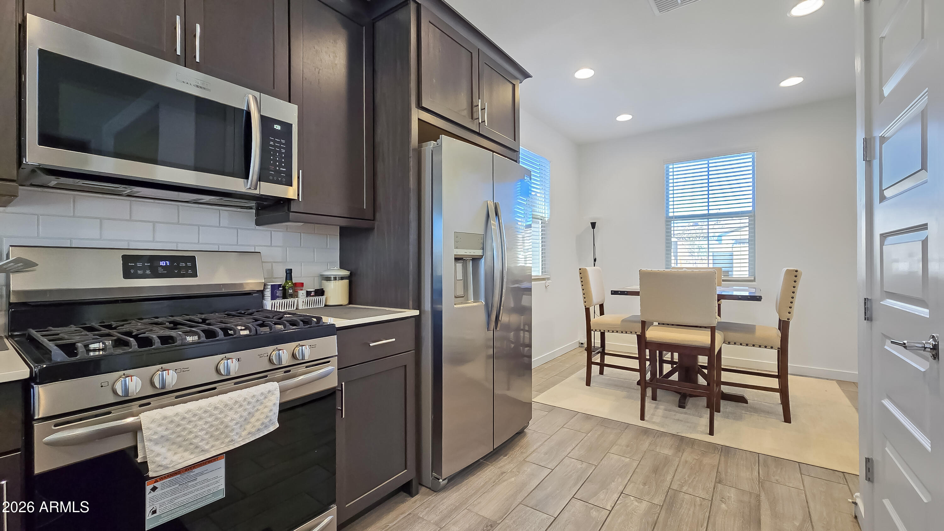 16839 West Evergreen Road Waddell, AZ 85355 - Photo 7 of 28 a kitchen with stainless steel appliances granite countertop a stove top oven a sink dishwasher a dining table and chairs with wooden floor