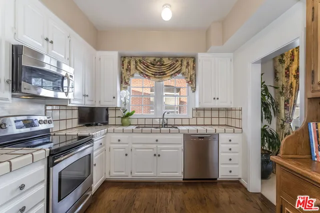 a kitchen with stainless steel appliances granite countertop a stove a sink dishwasher and white cabinets with wooden floor