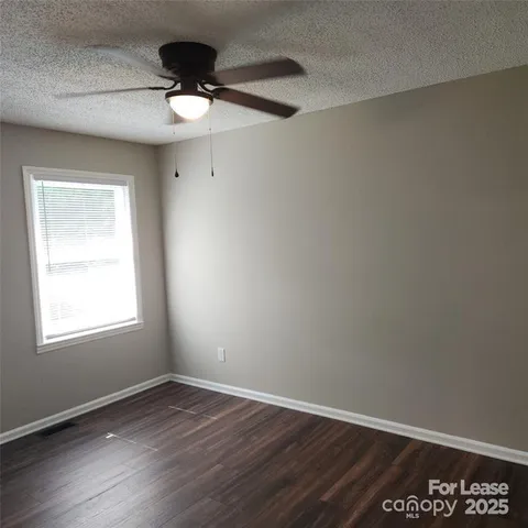 an empty room with wooden floor ceiling fan and window