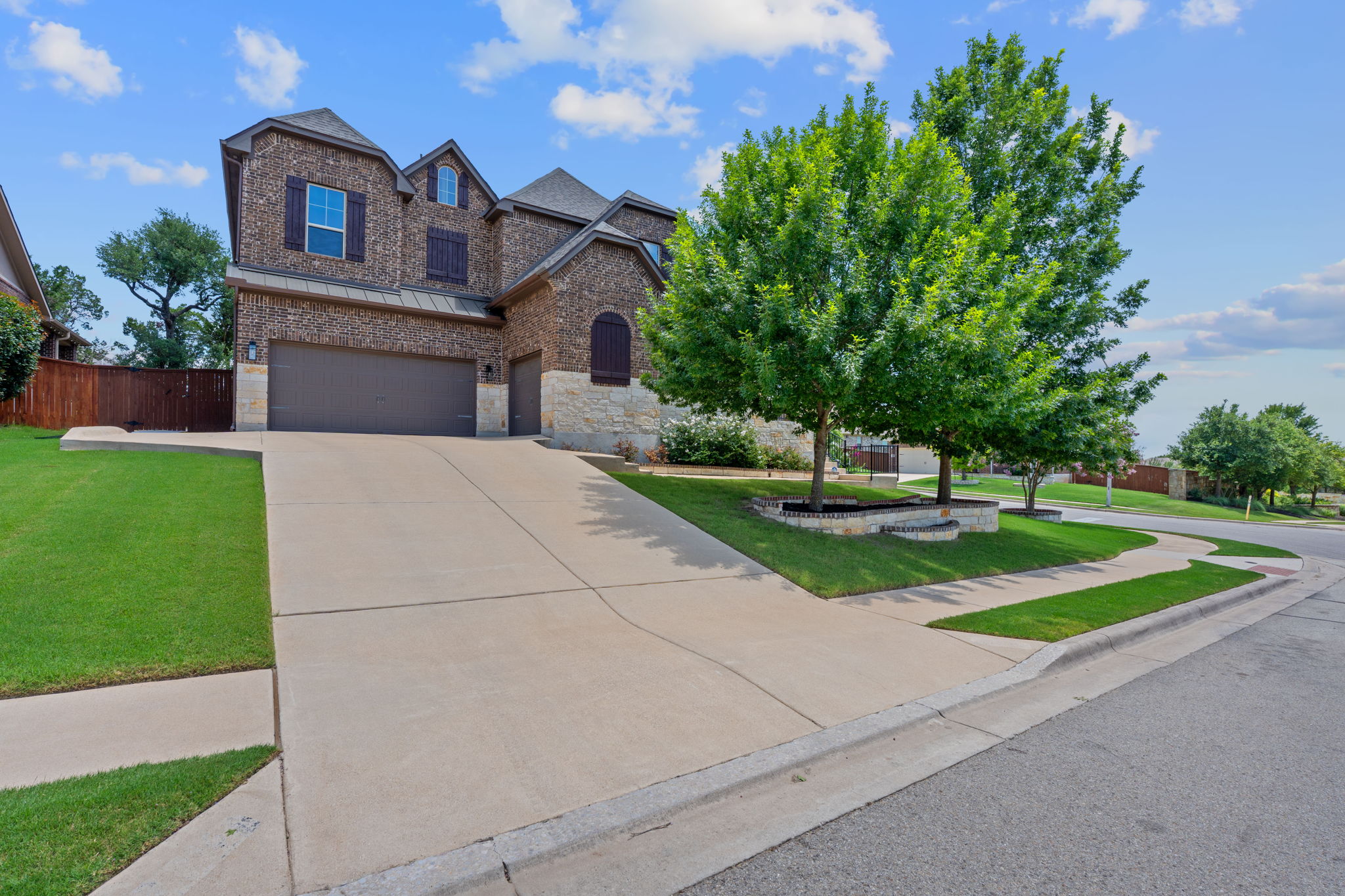 View of front facade with stone siding, a garage, brick siding, concrete driveway, and a standing seam roof