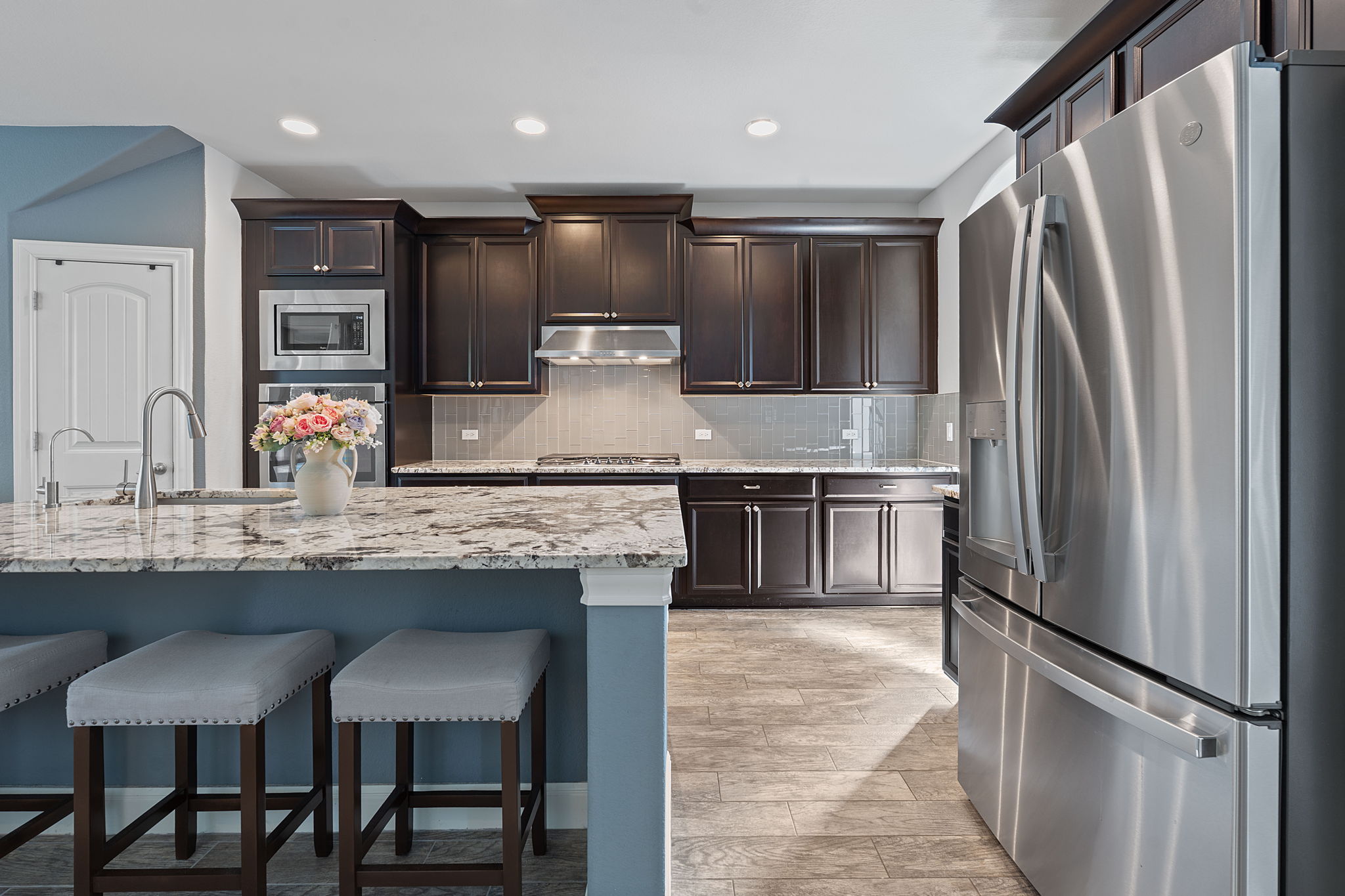 4212 Borho Ranch Street Leander, TX 78641 - Photo 4 of 37 Kitchen featuring stainless steel appliances, dark brown cabinets, a kitchen bar, tasteful backsplash, and ventilation hood
