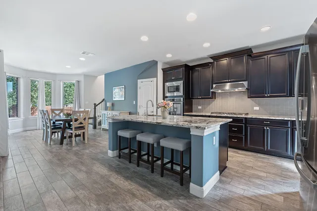 a kitchen with stainless steel appliances granite countertop a stove top oven a sink a dining table and chairs