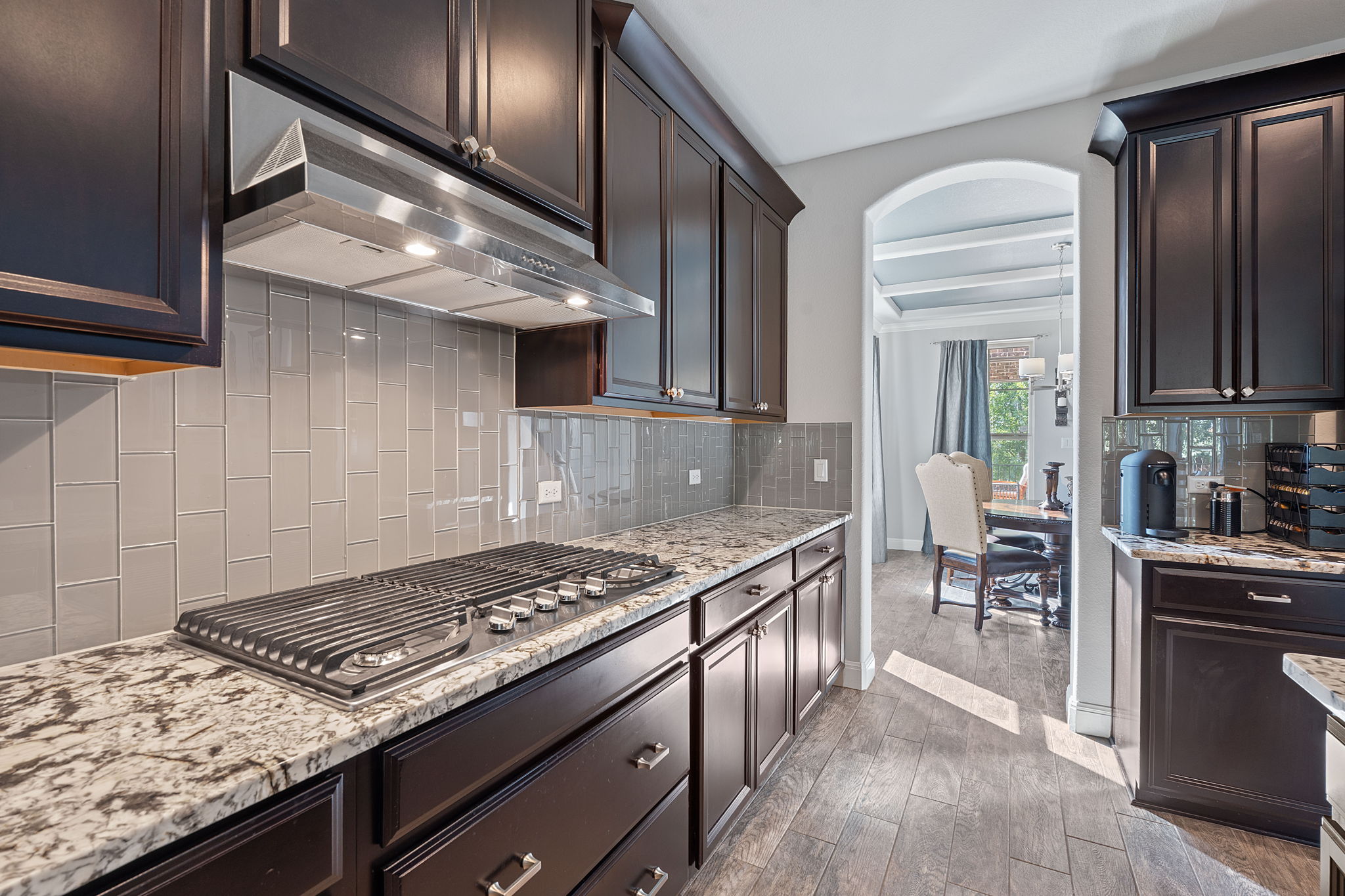 4212 Borho Ranch Street Leander, TX 78641 - Photo 8 of 37 Kitchen featuring under cabinet range hood, backsplash, stainless steel gas cooktop, wood finished floors, and beamed ceiling