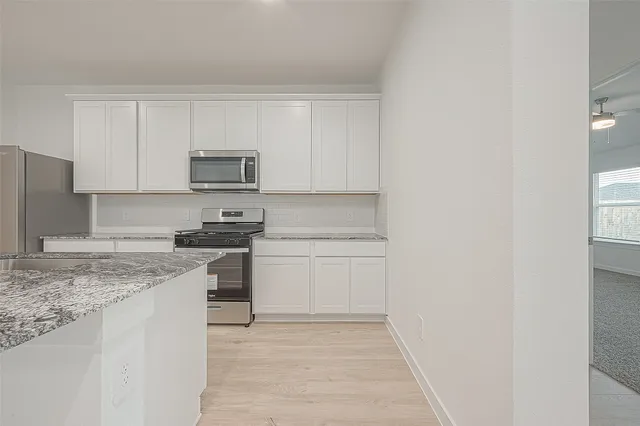 a kitchen with stainless steel appliances granite countertop a stove top oven a sink and white cabinets