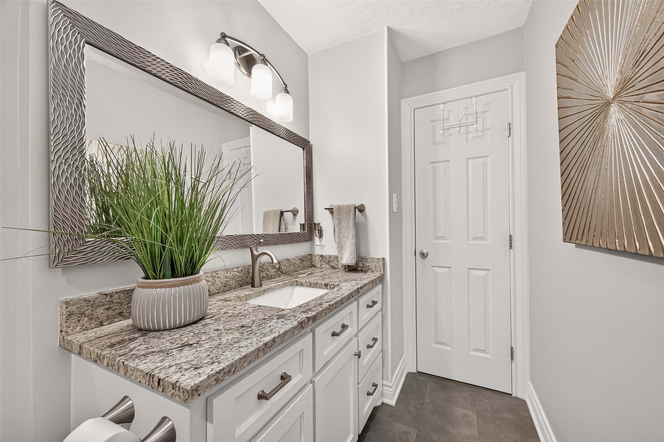 24719 Wilderness Road Spring, TX 77380 - Photo 24 of 42 This bathroom features a modern design with a granite countertop, sleek white cabinetry, and a large decorative mirror. It includes elegant lighting and stylish decor, creating a fresh and inviting space.