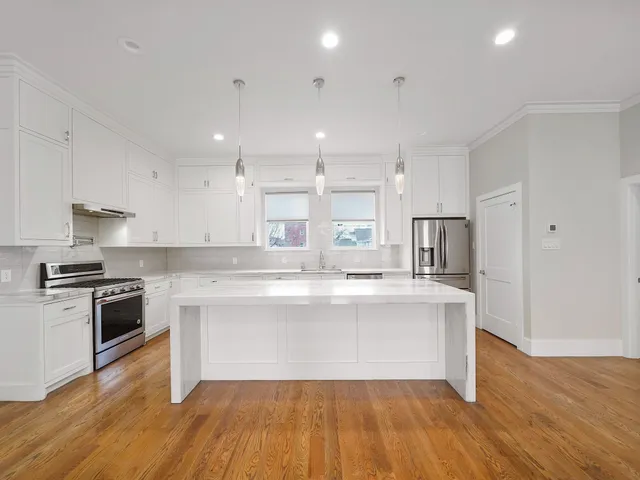 a large kitchen with kitchen island a stove a sink wooden floor and a refrigerator