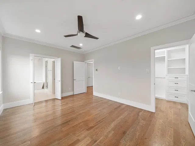 a view of an empty room with wooden floor and a ceiling fan