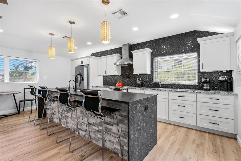 2476 North Beach Road Englewood, FL 34223 - Photo 12 of 58 a large kitchen with stainless steel appliances kitchen island granite countertop a stove a sink a dining table and chairs with wooden floor