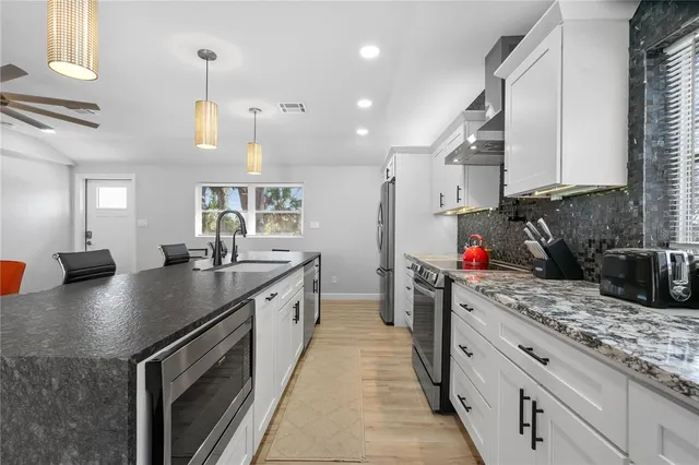 a kitchen with stainless steel appliances granite countertop a sink a stove and a wooden cabinets