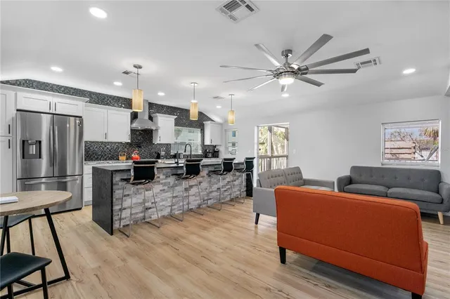 a kitchen with stainless steel appliances kitchen island granite countertop a refrigerator a stove a sink a dining table and chairs with wooden floor