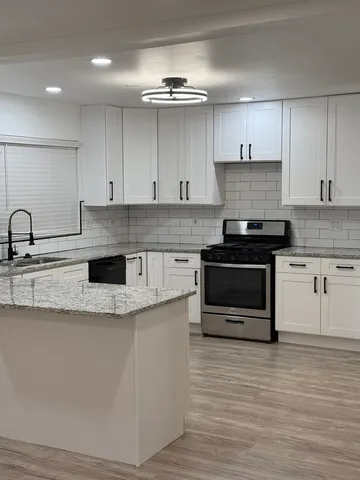 a kitchen with kitchen island granite countertop a stove top oven a sink and cabinets