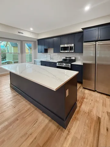 a large kitchen with kitchen island a sink dishwasher a refrigerator and a stove with wooden floor