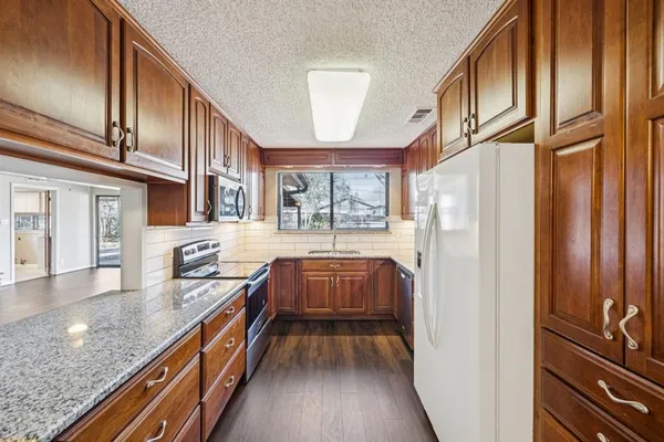 a kitchen with granite countertop a refrigerator a sink dishwasher stove and wooden cabinets