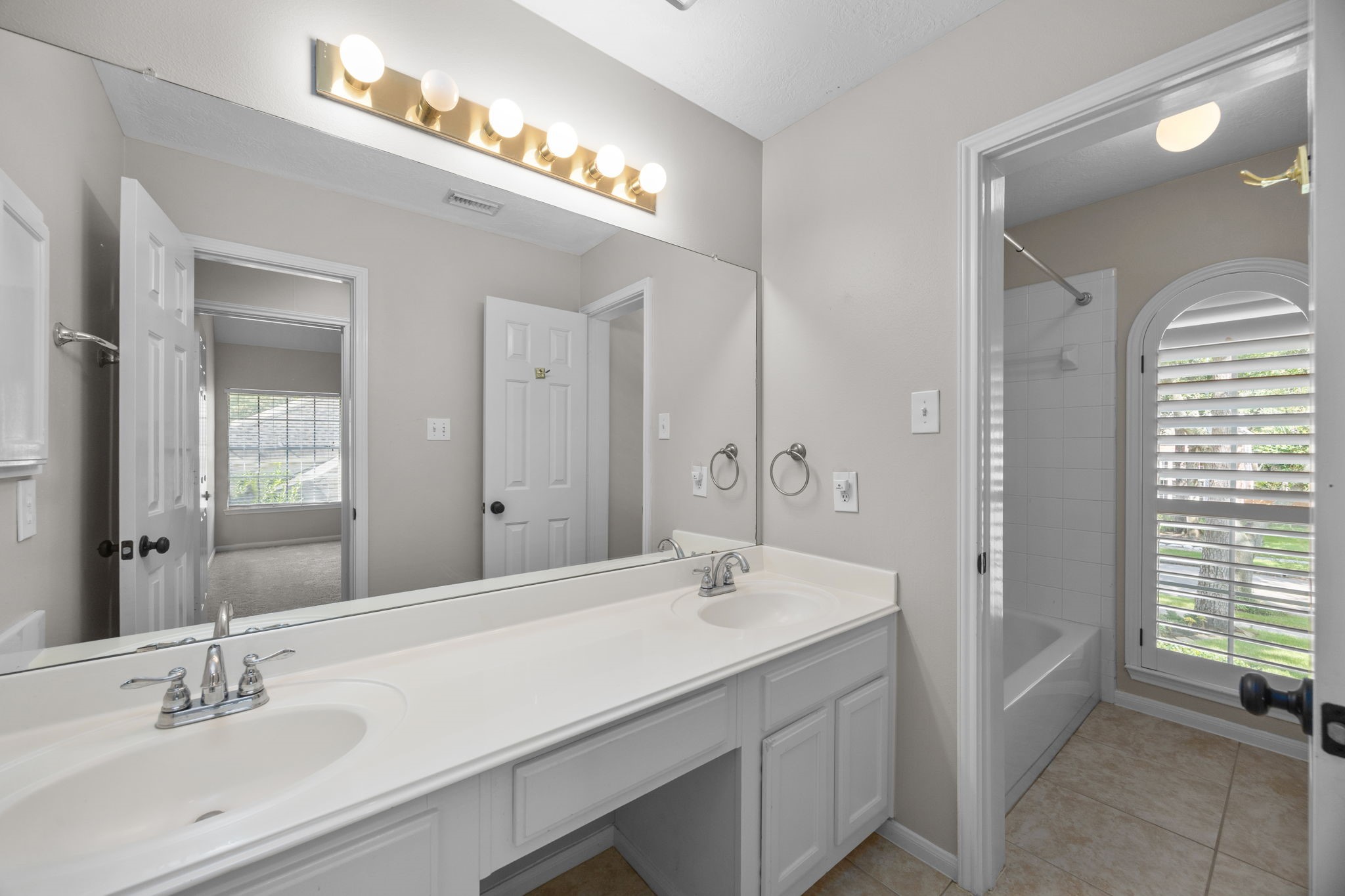 9015 Rhapsody Lane Houston, TX 77040 - Photo 30 of 39 Upstairs secondary bathroom featuring a double-sink vanity with generous counter space and a separate tub/shower area. A large arched window with plantation shutters brings in plenty of natural light.
