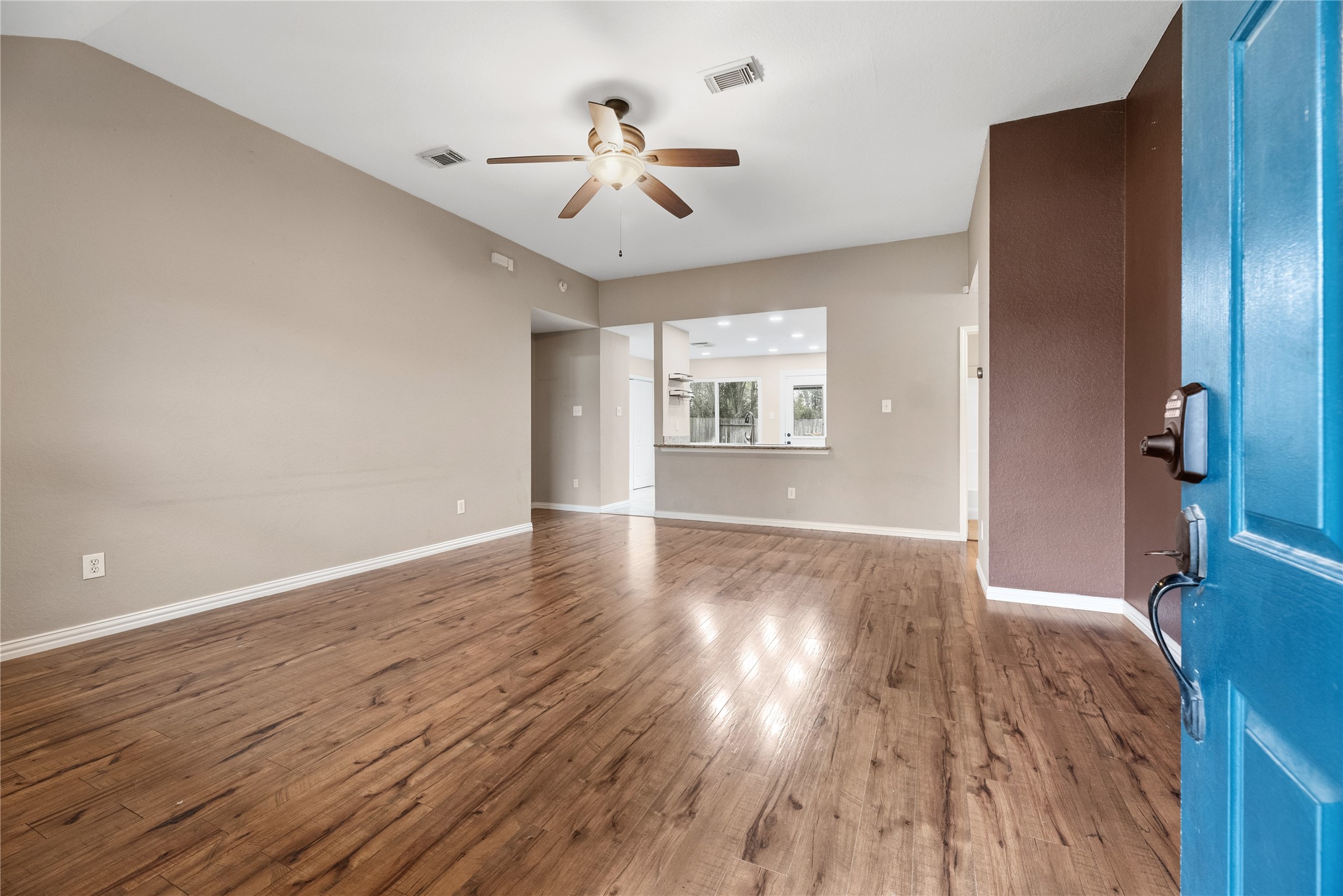 24006 Lazy Kay Lane Hockley, TX 77447 - Photo 4 of 21 This photo shows a spacious living area with gorgeous floors, neutral walls, and a ceiling fan. The room opens to a kitchen with a breakfast bar, visible through an open concept layout.