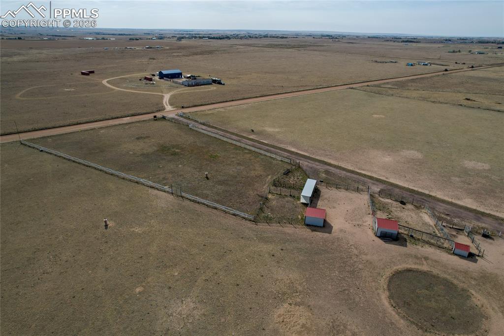 7880 J D Johnson Road Peyton, CO 80831 - Photo 30 of 50 Expansive rural property featuring an established gravel drive, fenced pastures, multiple outbuildings with red roofs, and a large blue barn structure