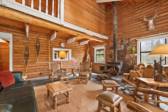 4725 Pine Ridge Road Evanston, UT 82930 - Photo 8 of 82 Expansive living area showcasing wood-finish log walls and ceilings, a prominent stone fireplace with a wood-burning stove, large windows, and a carpeted floor