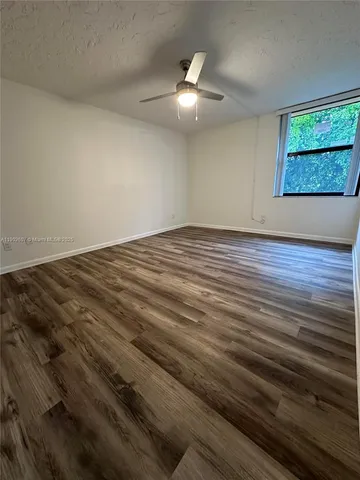 an empty room with wooden floor chandelier fan and windows