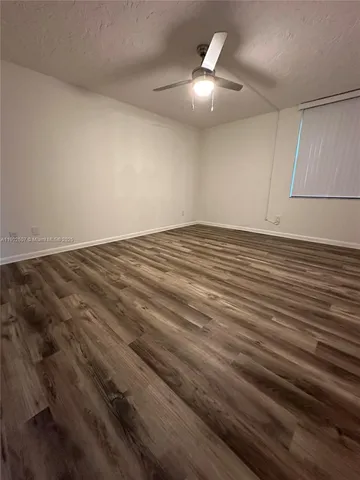 an empty room with wooden floor fan and window