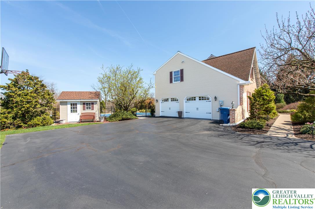 4059 Old Sentry Road Allentown, PA 18104 - Photo 36 of 39 A spacious asphalt driveway leads to a two-car garage and a charming detached shed, all nestled under clear skies.