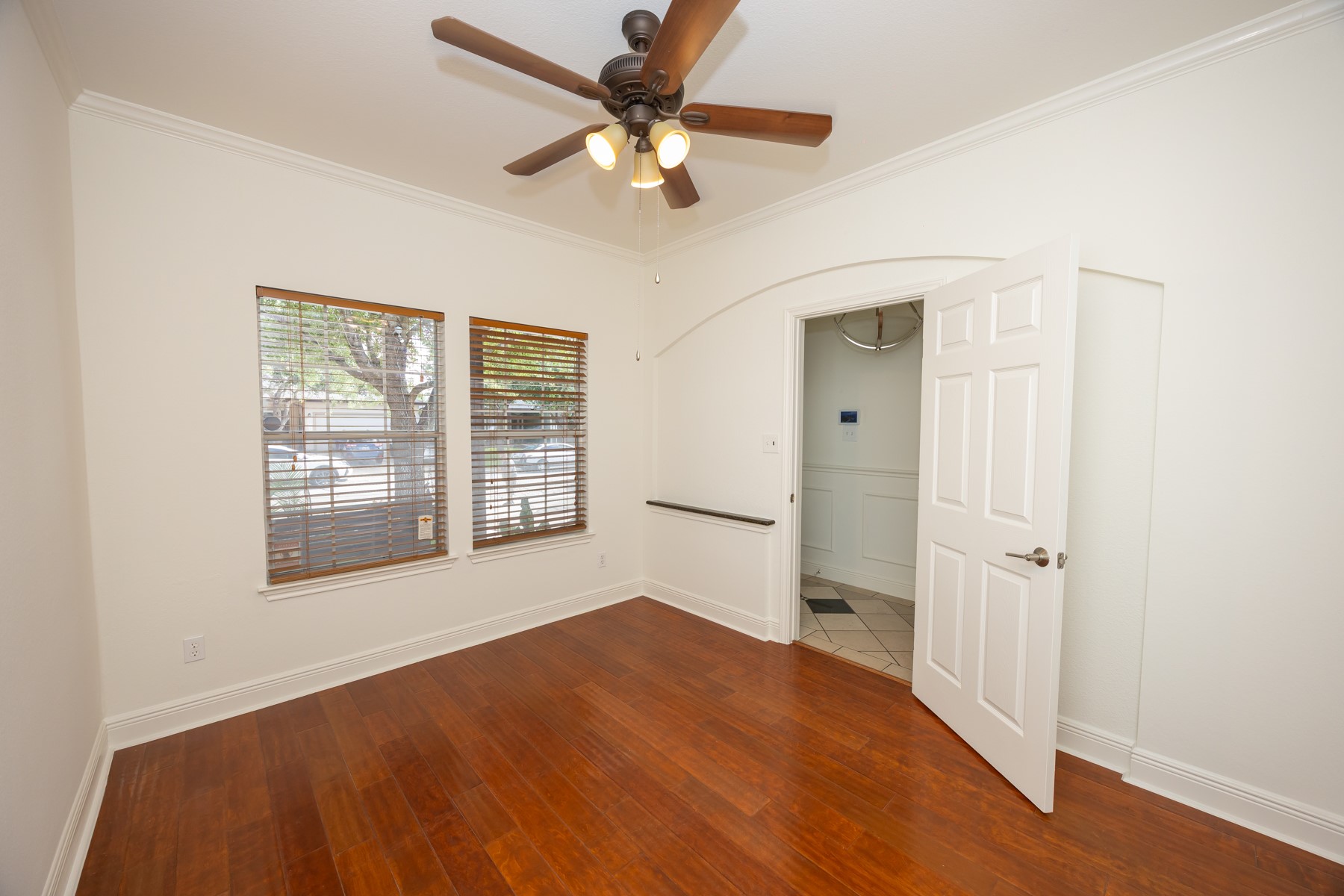 11500 Dimmit Street Manor, TX 78653 - Photo 3 of 14 Room featuring hardwood flooring, crown molding, two windows with wood blinds, an arched doorway, and a ceiling fan with integrated lighting