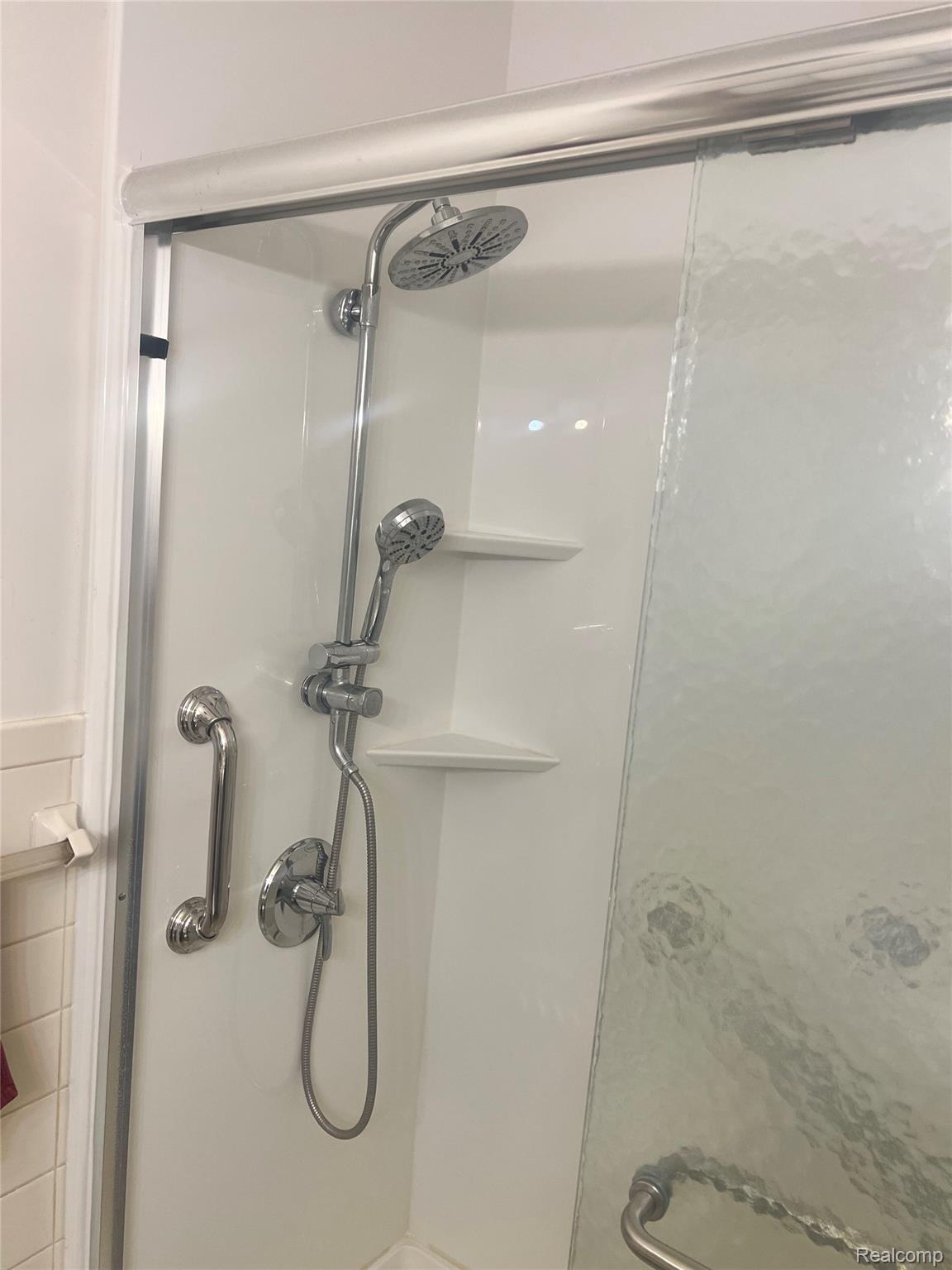 3063 West Britton Road Perry, MI 48872 - Photo 17 of 32 Shower enclosure with white surround, rainfall showerhead, handheld shower fixture, and integrated shelving