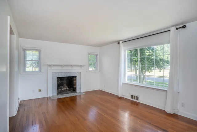 an empty room with wooden floor fireplace and windows