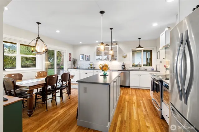 a kitchen with stainless steel appliances kitchen island granite countertop a table chairs and a wooden floor
