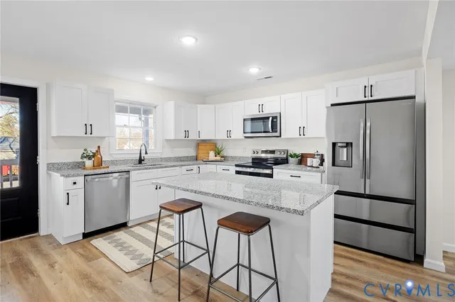 a kitchen with stainless steel appliances granite countertop a refrigerator a stove a sink dishwasher and white cabinets with wooden floor