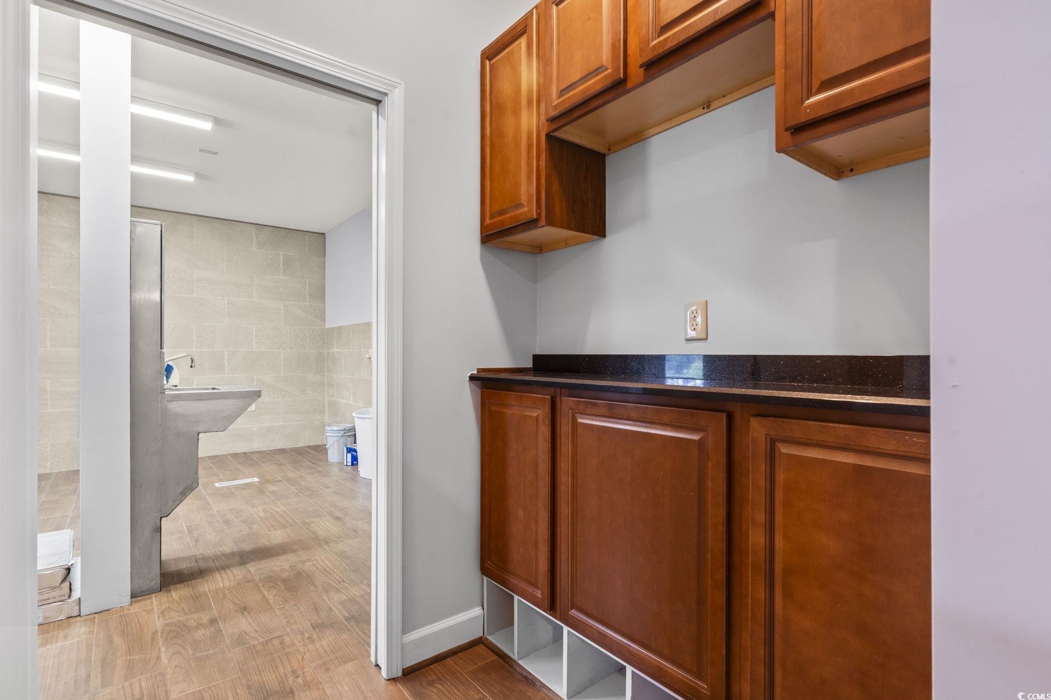 1585 Daisy Road Loris, SC 29569 - Photo 22 of 39 Bar with brown cabinets, tile walls, light wood-style flooring, and dark stone countertops