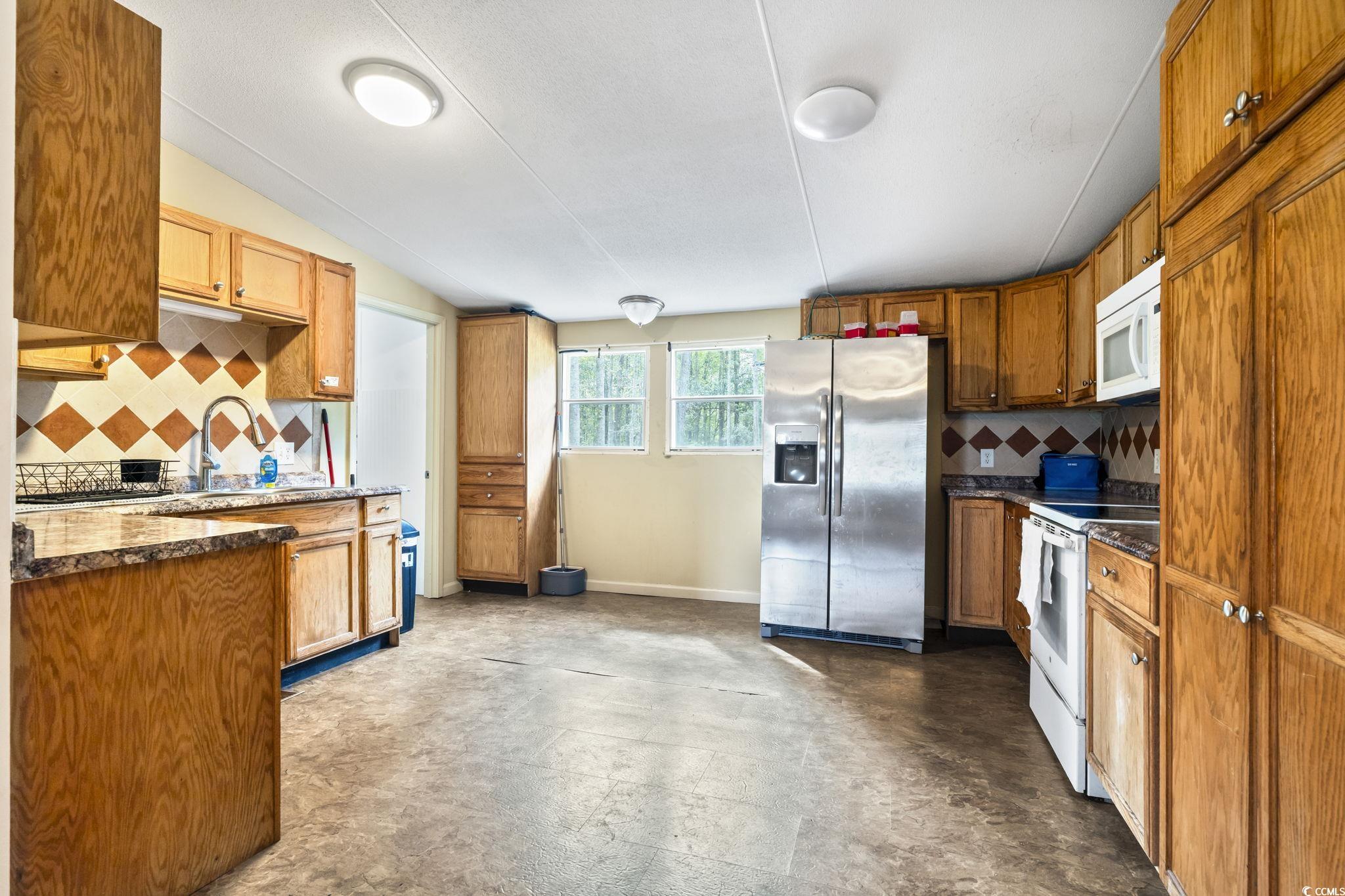 1585 Daisy Road Loris, SC 29569 - Photo 28 of 39 Kitchen with tasteful backsplash, white appliances, brown cabinetry, vaulted ceiling, and dark stone countertops