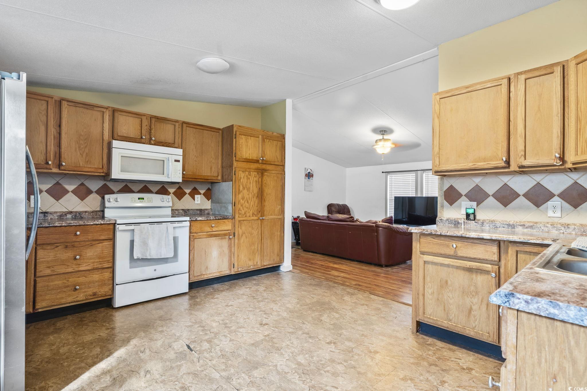 1585 Daisy Road Loris, SC 29569 - Photo 39 of 39 Kitchen with decorative backsplash, white appliances, open floor plan, lofted ceiling, and brown cabinetry