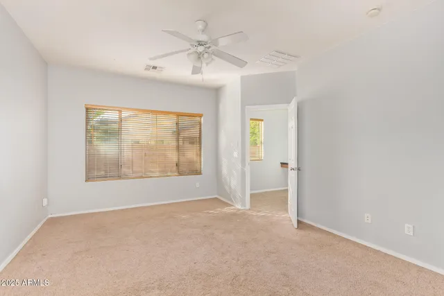 an empty room with chandelier fan and windows