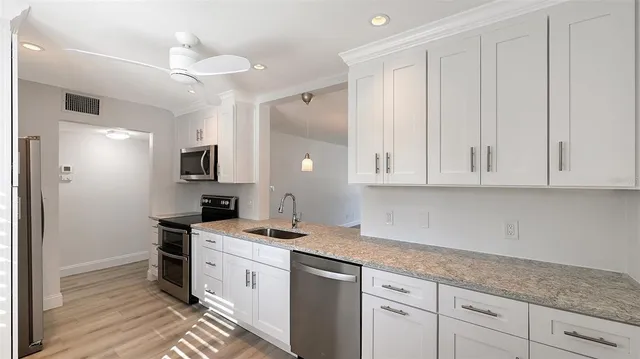 a kitchen with a sink dishwasher and white cabinets with wooden floor