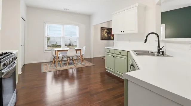 a kitchen with stainless steel appliances granite countertop a stove top oven a sink a dining table and chairs with wooden floor