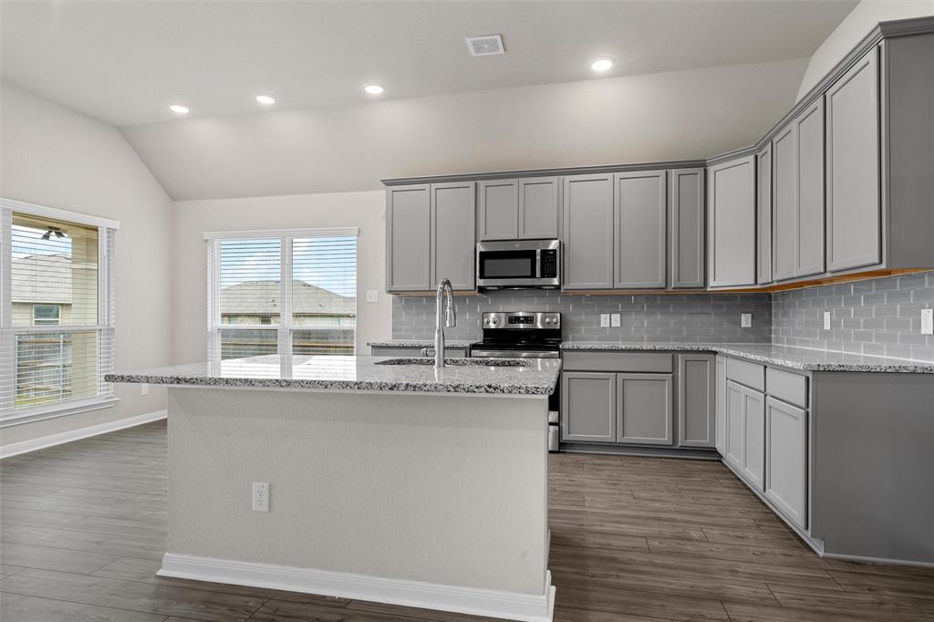 3208 Dottavio Road Lorena, TX 76655 - Photo 11 of 31 Kitchen featuring an island with a breakfast bar, granite countertops, gray shaker-style cabinetry, stainless steel appliances, and wood-finish flooring