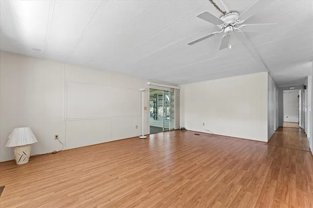 a view of an empty room with wooden floor and a ceiling fan