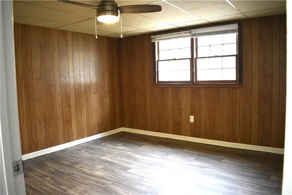 an empty room with wooden floor chandelier fan and windows