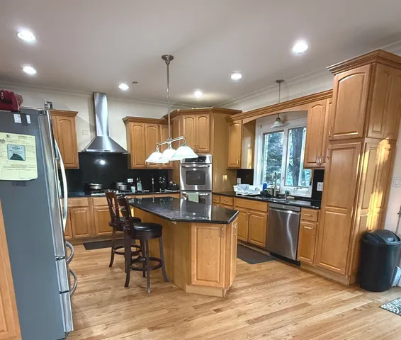 a kitchen with stainless steel appliances granite countertop a refrigerator a stove a sink a dining table and chairs with wooden floor