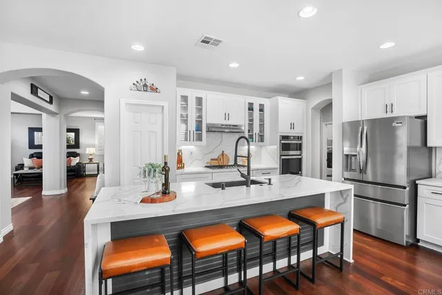 a kitchen with stainless steel appliances granite countertop a dining table chairs refrigerator and stove